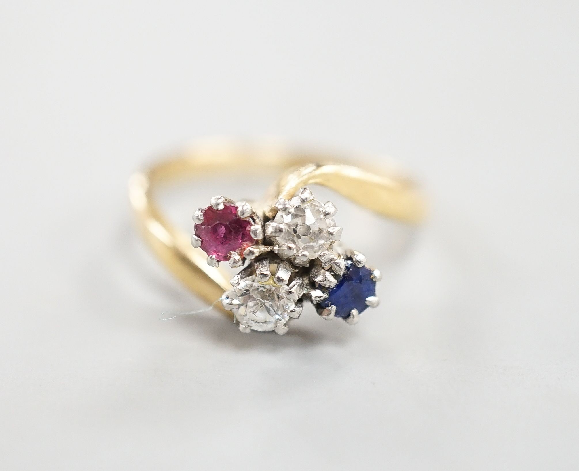 An early 20th century 18ct & plat, ruby, sapphire and diamond set four stone crossover ring, size M, gross weight 4 grams.